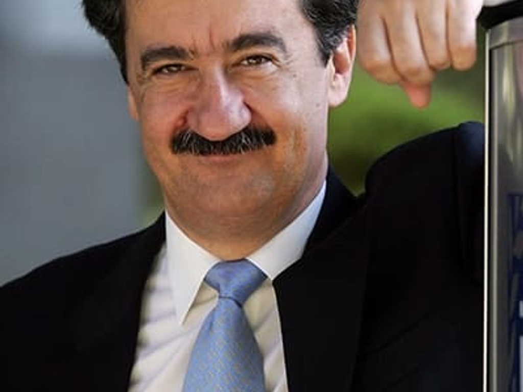 A man in a suit with a mustache smiling and leaning on a railing.