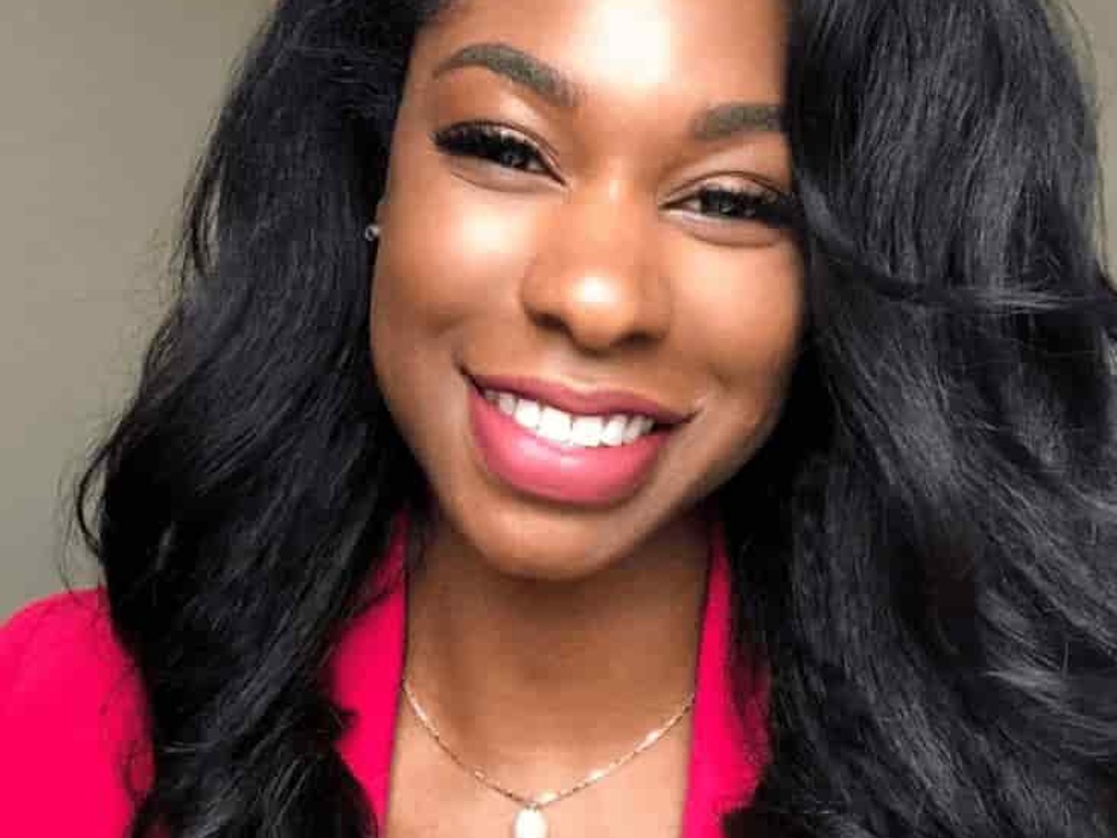 A portrait of a smiling woman with long black hair wearing a pink blazer.