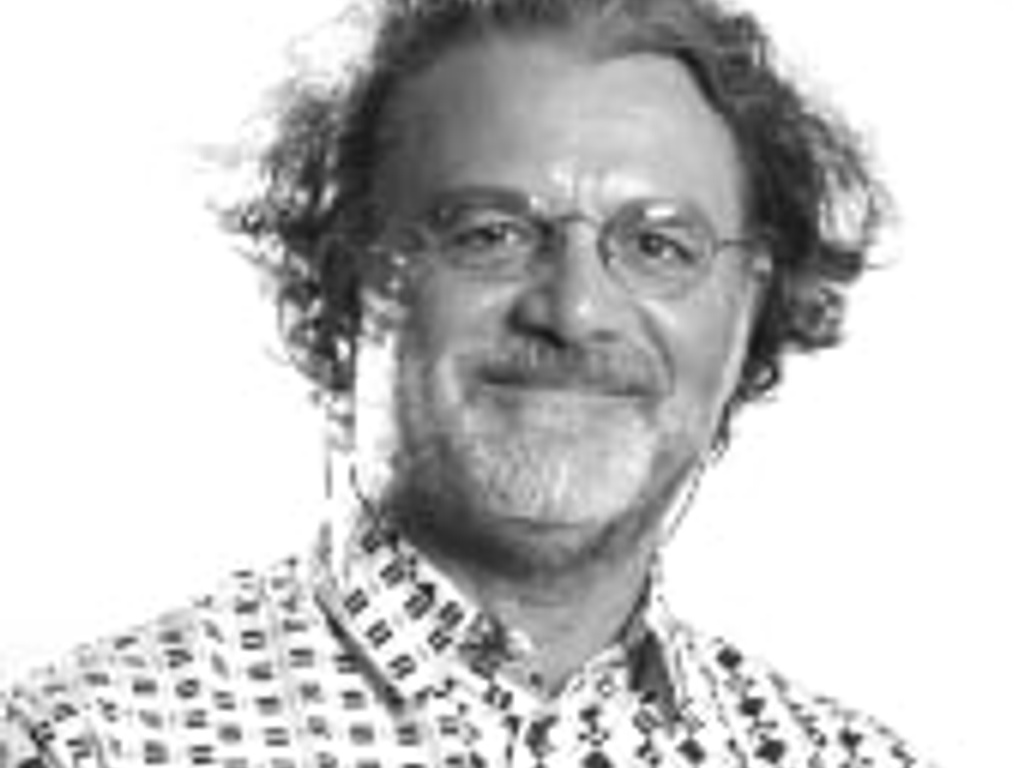 A black and white portrait of a smiling middle-aged man with curly hair and glasses, wearing a patterned shirt.