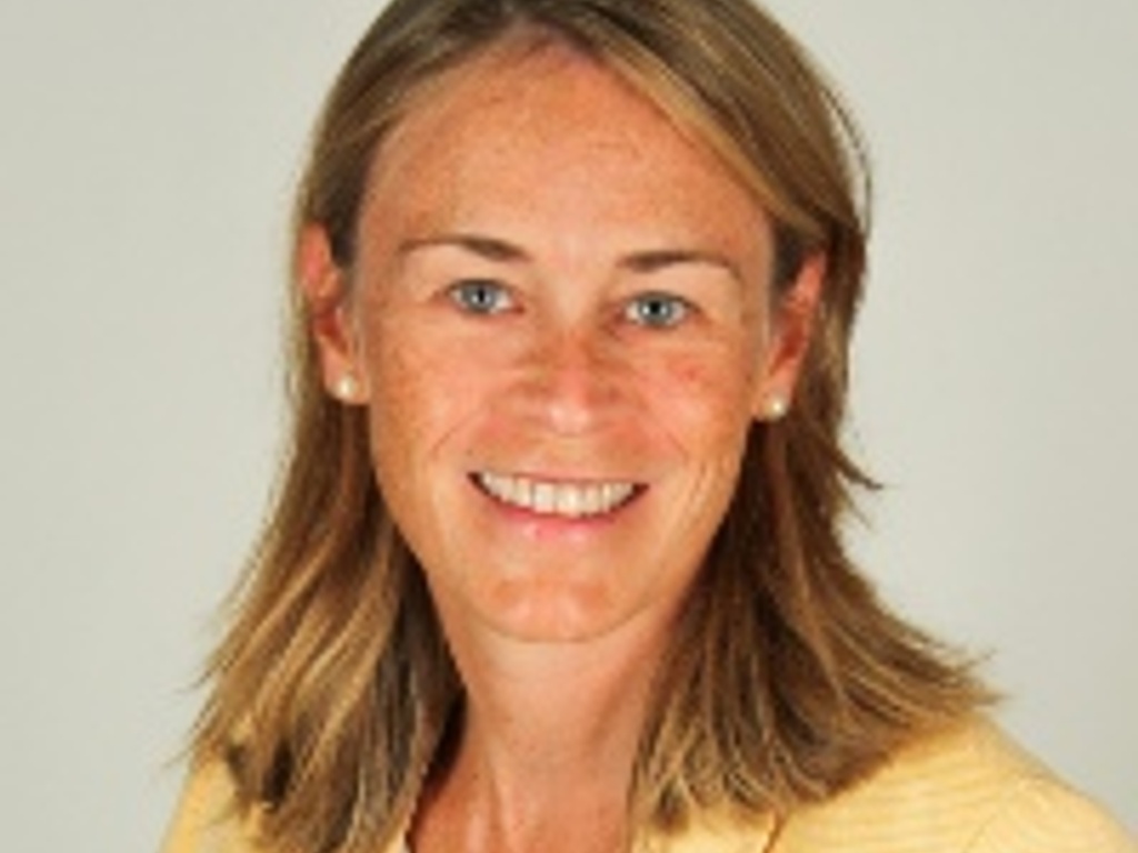 A portrait of a smiling woman with blonde hair wearing a yellow jacket.