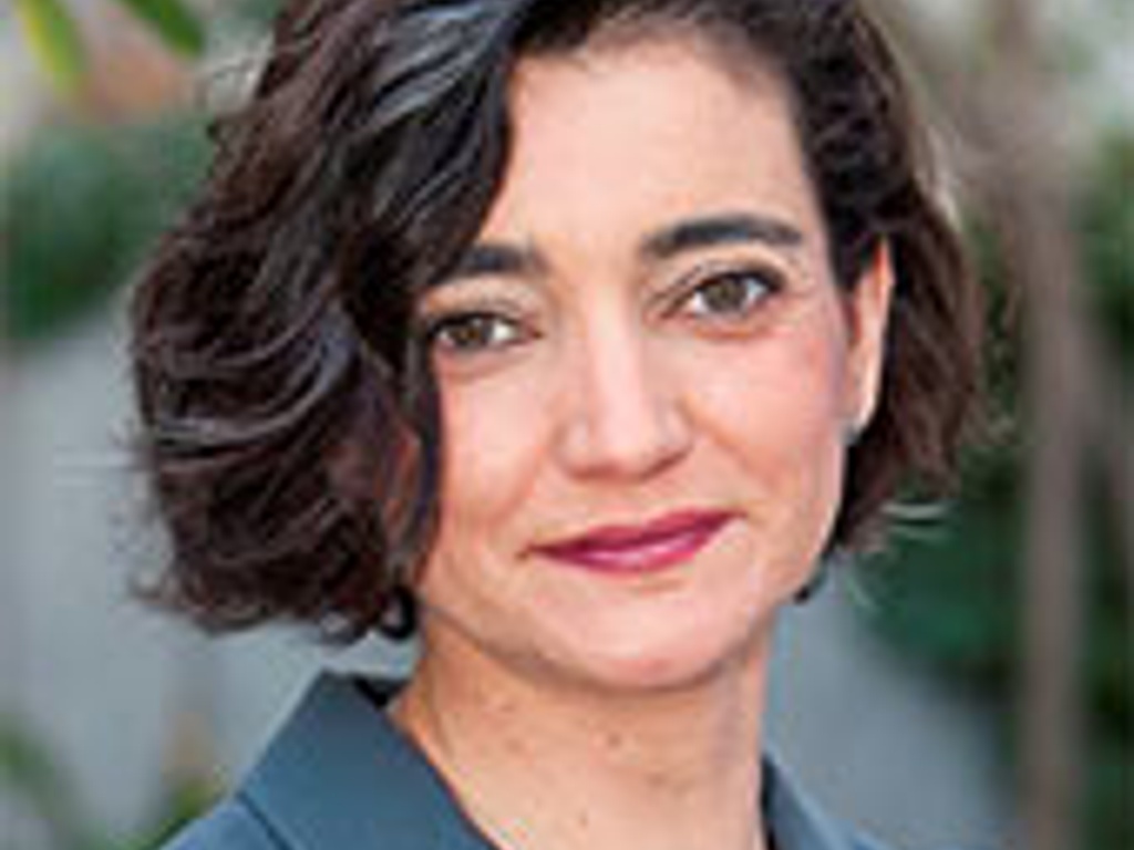 A portrait of a middle-aged woman with short curly hair, smiling slightly against a blurred greenery background.