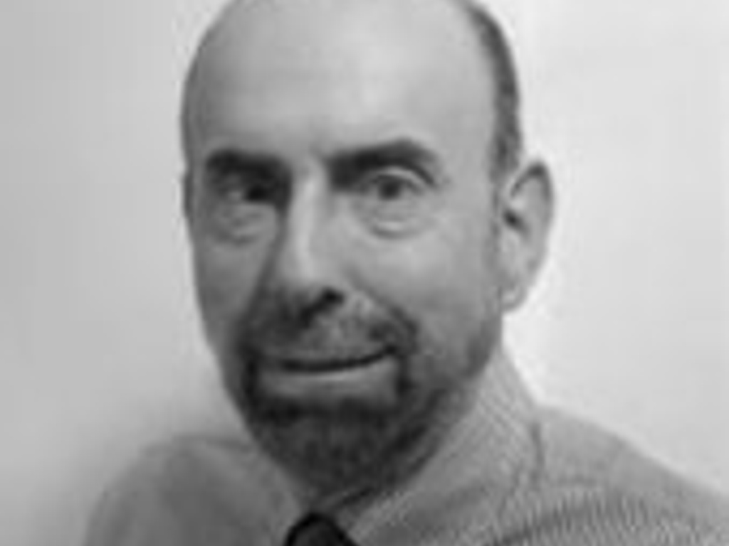 A black and white headshot of a smiling bald man wearing a tie.