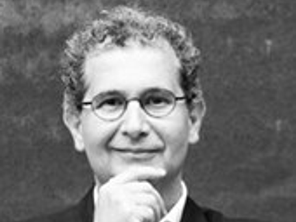 Black and white portrait of a middle-aged man with curly hair, wearing glasses and a suit, posing with his hand on his chin.