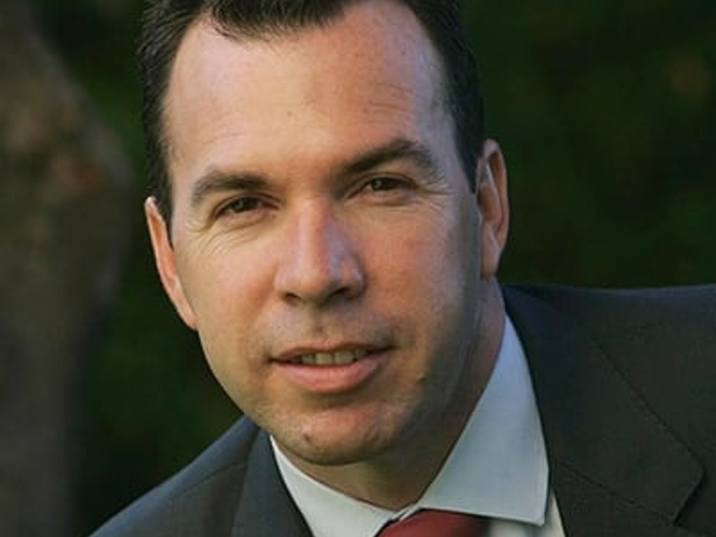 A portrait of a man in a suit with a red tie, looking directly at the camera.