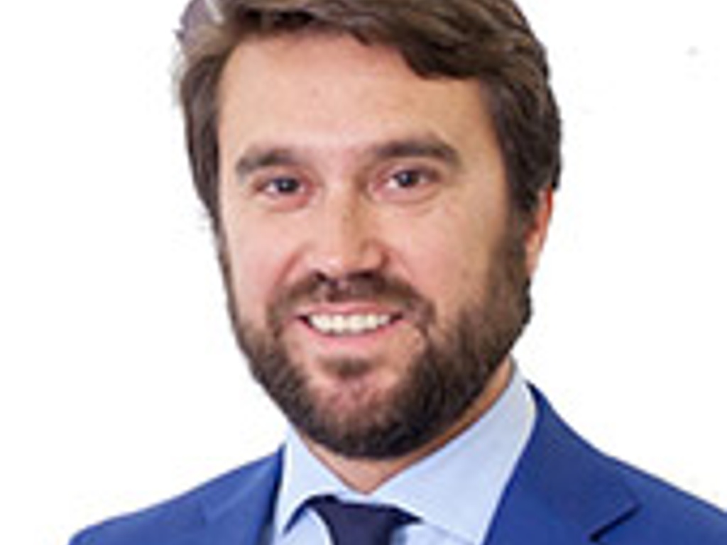 Professional portrait of a smiling man with a beard, wearing a blue suit and tie.