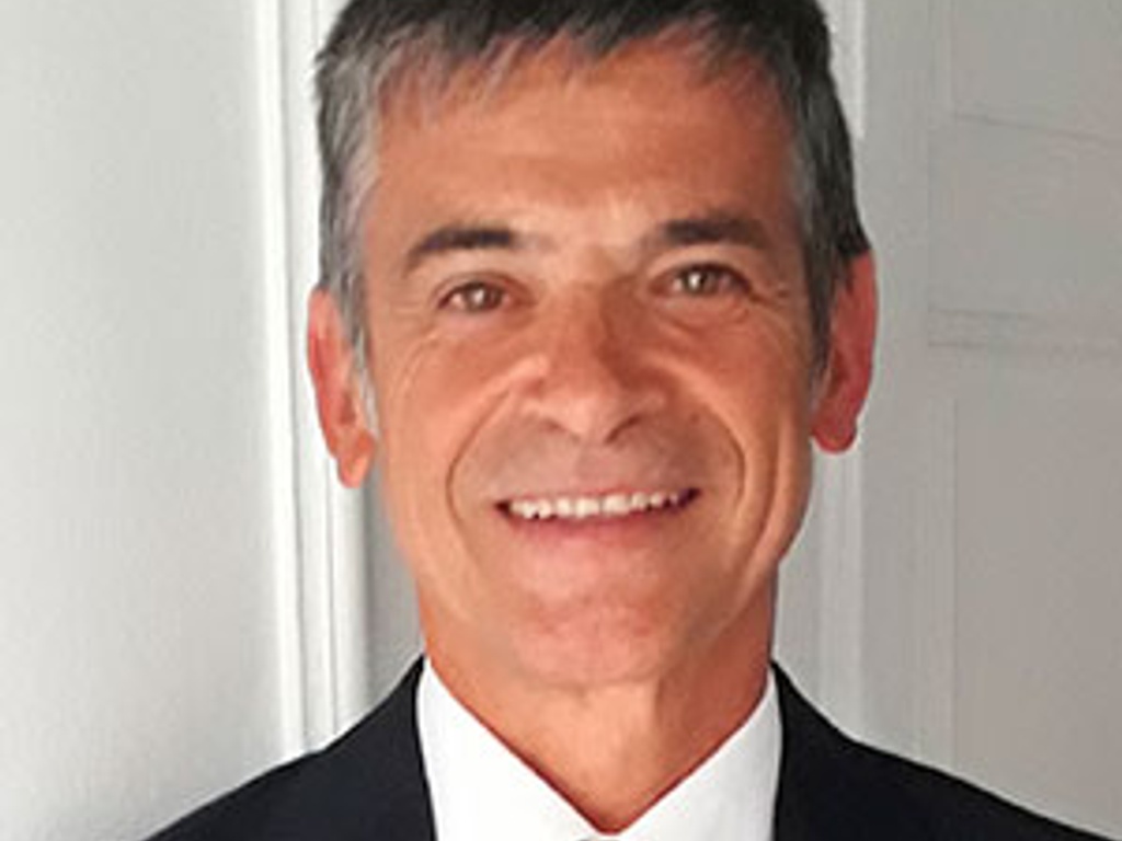 A portrait of a smiling man wearing a red tie and dark suit.