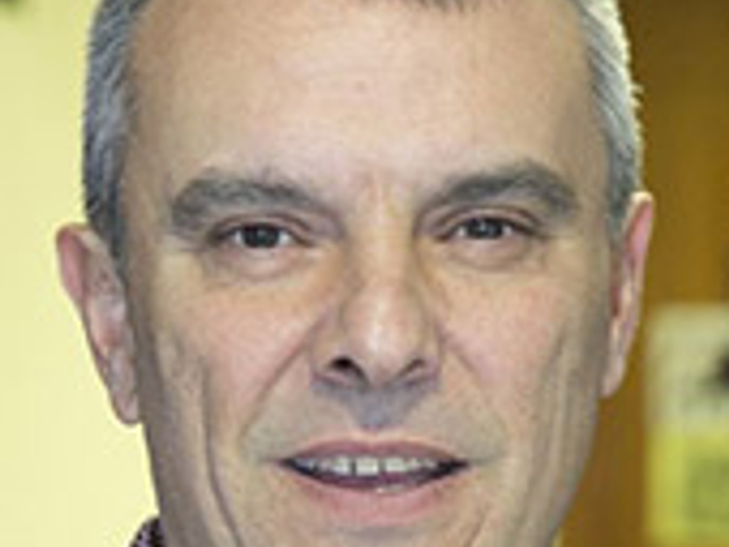 A close-up portrait of a smiling middle-aged man with short gray hair