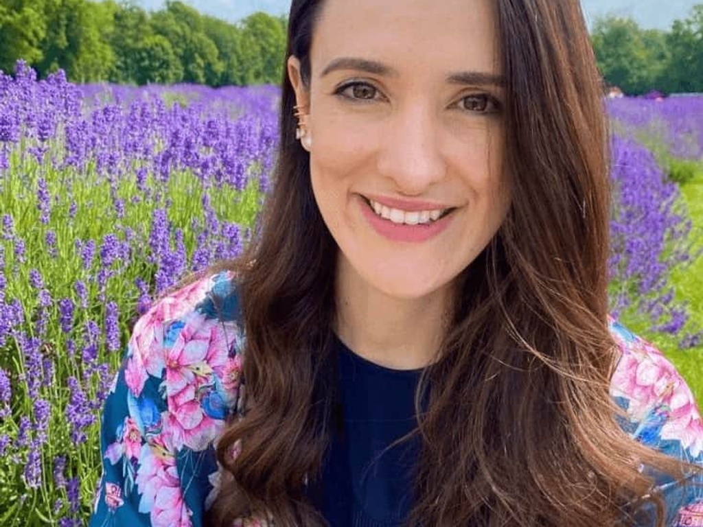 A woman smiling in a field of purple lavender under a clear blue sky.