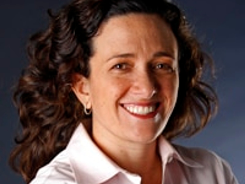 A portrait of a smiling woman with curly hair wearing a white shirt against a blue background.