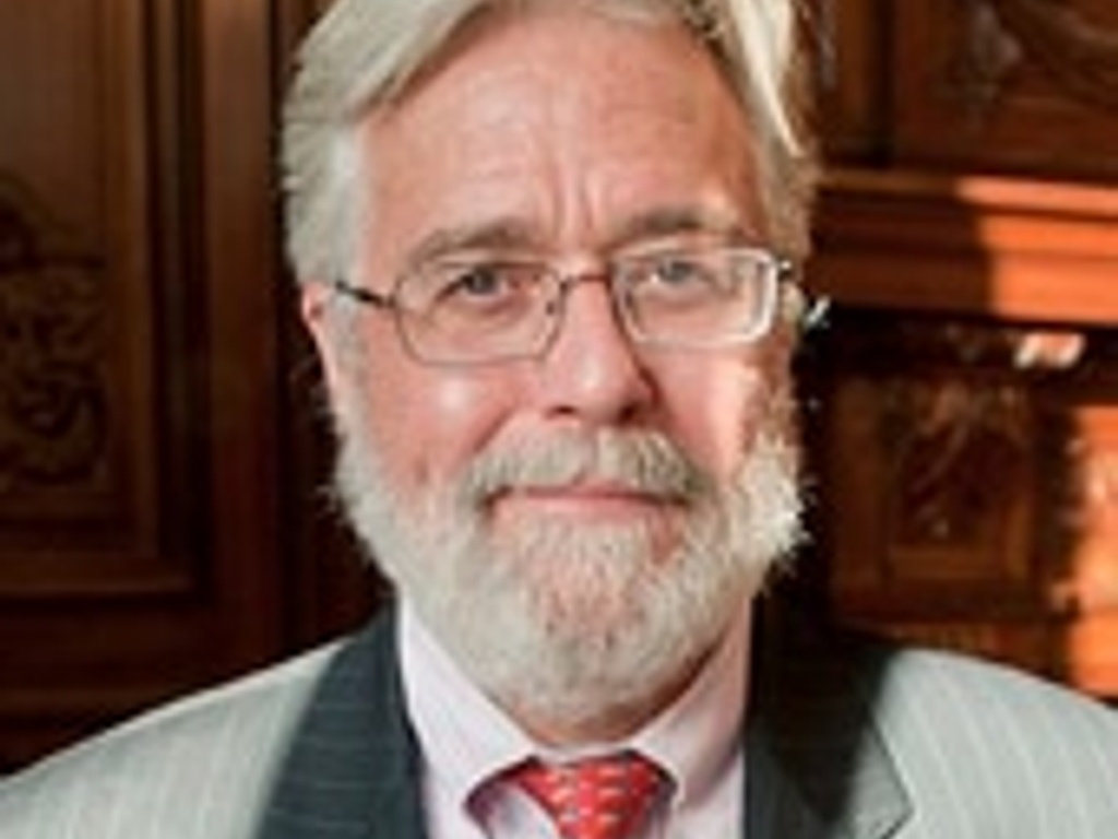 A portrait of an elderly man with a white beard, wearing glasses, a suit, and a red tie.