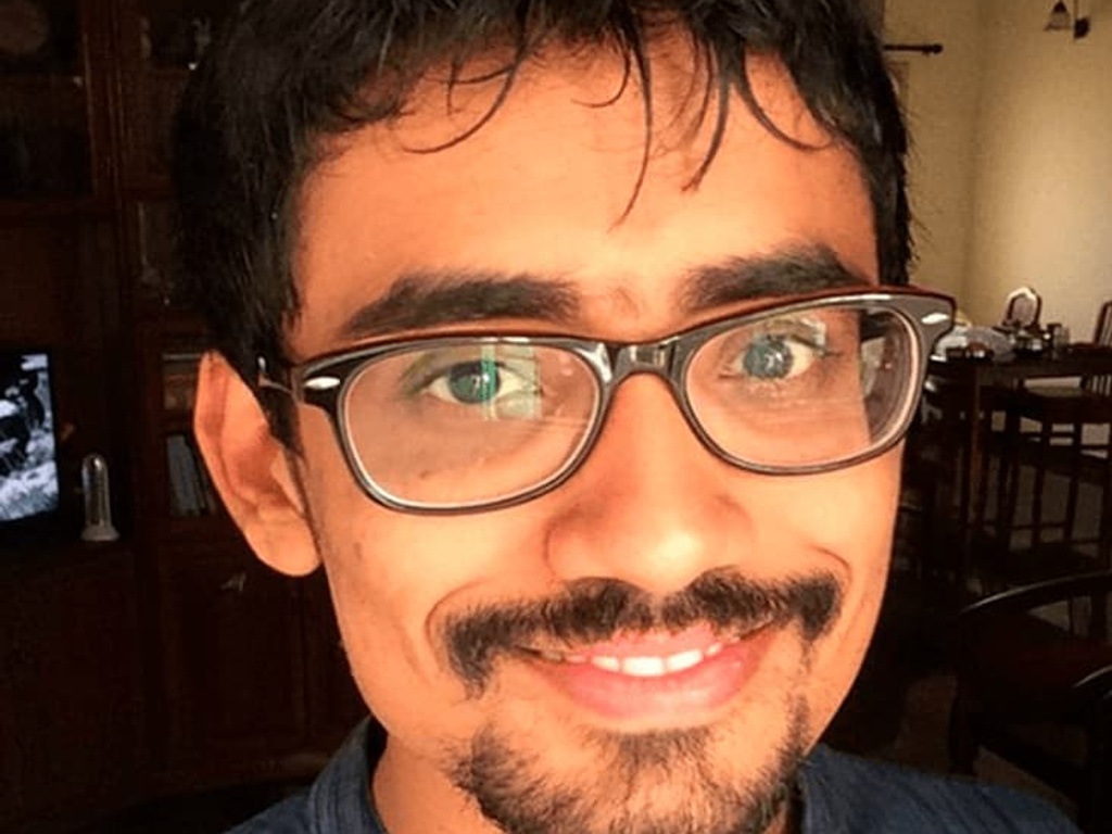 A portrait of a smiling man with glasses wearing a blue shirt.