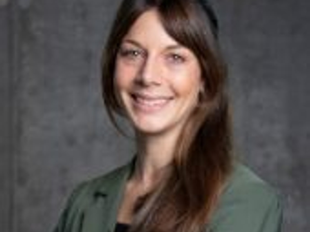 A professional portrait of a smiling woman with long hair wearing a green blazer.