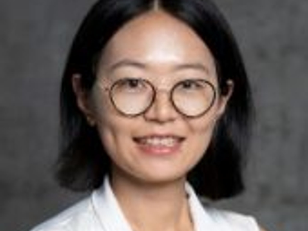 A portrait of a smiling woman with round glasses wearing a white top.