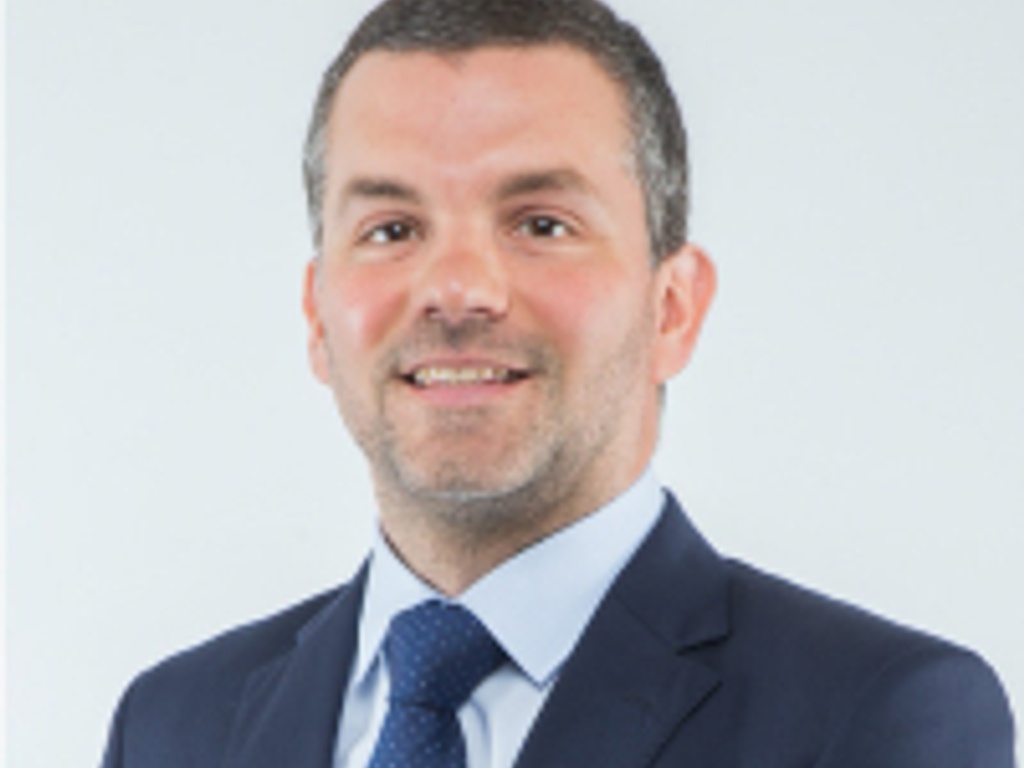 A professional portrait of a smiling man wearing a blue suit and tie.