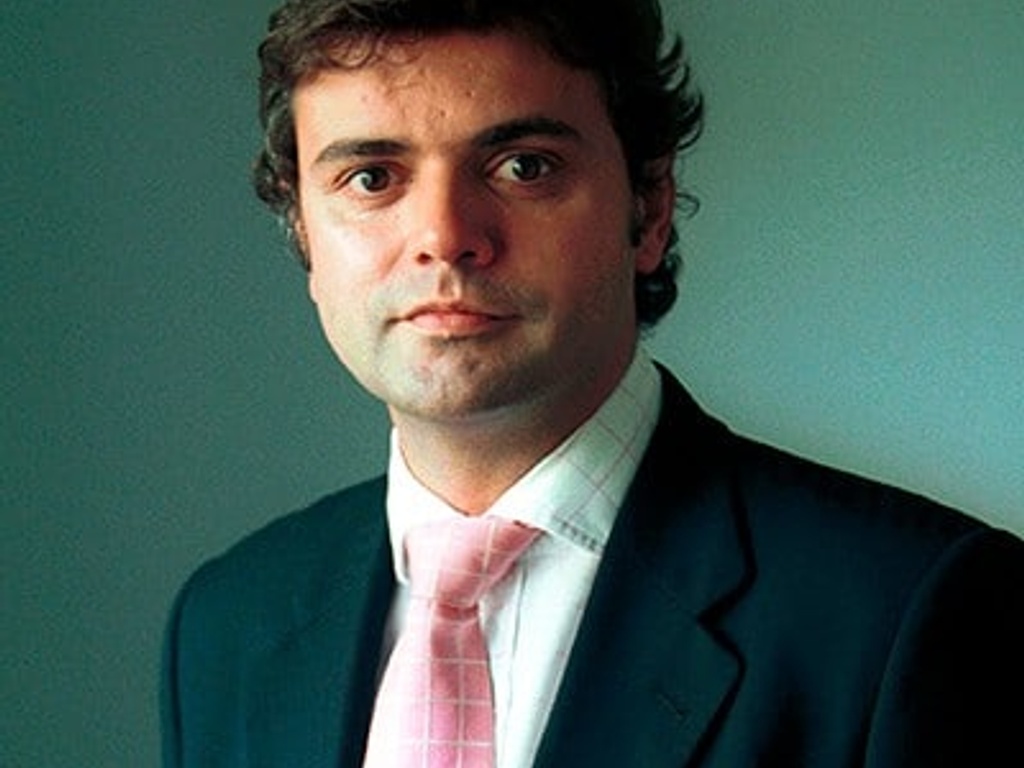 Portrait of a man in a business suit with a pink tie and dark hair looking slightly to his left.