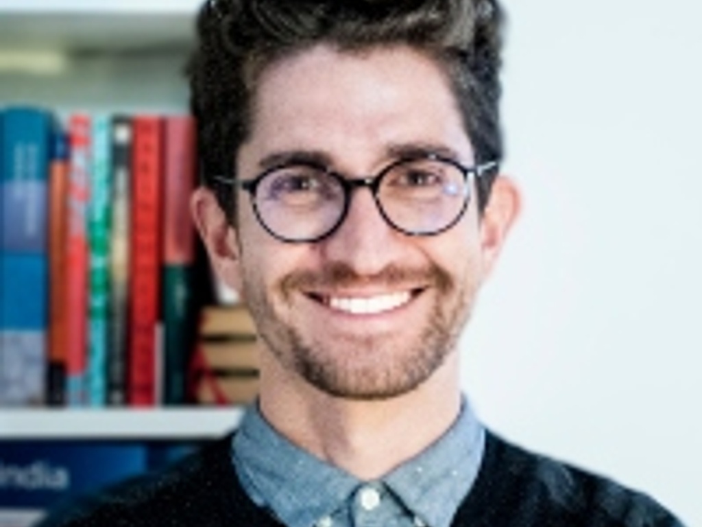 A smiling man with glasses standing in front of a bookshelf.