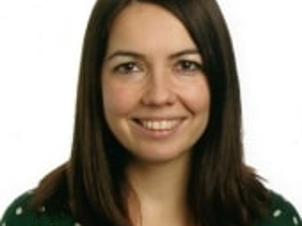 A portrait of a smiling woman with long brown hair, wearing a green polka dot blouse.