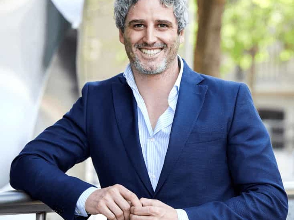 A smiling man in a blue suit standing outdoors with a casual posture.