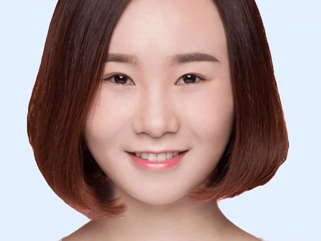 A portrait of a young woman with shoulder-length brown hair and a gentle smile, against a light blue background.