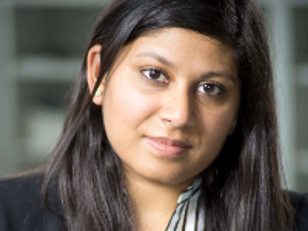 Portrait of a woman with long hair, wearing a dark blazer and a striped shirt, looking at the camera.