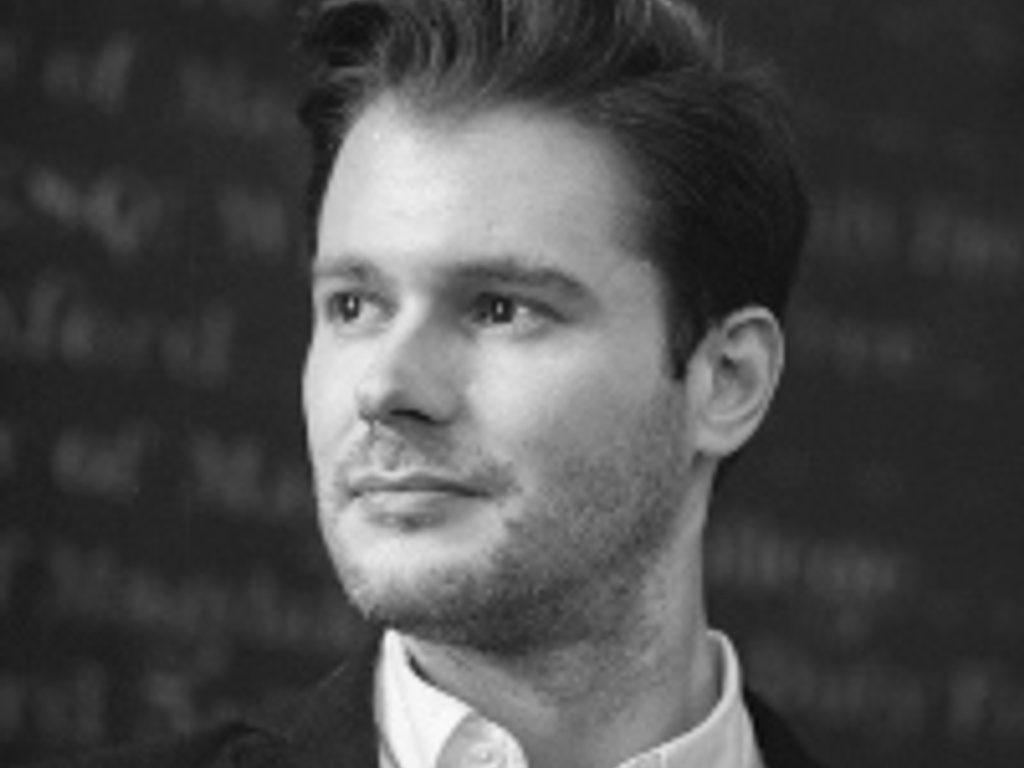 Black and white portrait of a young man with a thoughtful expression, dressed in a formal shirt and jacket, standing against a background with mathematical equations.