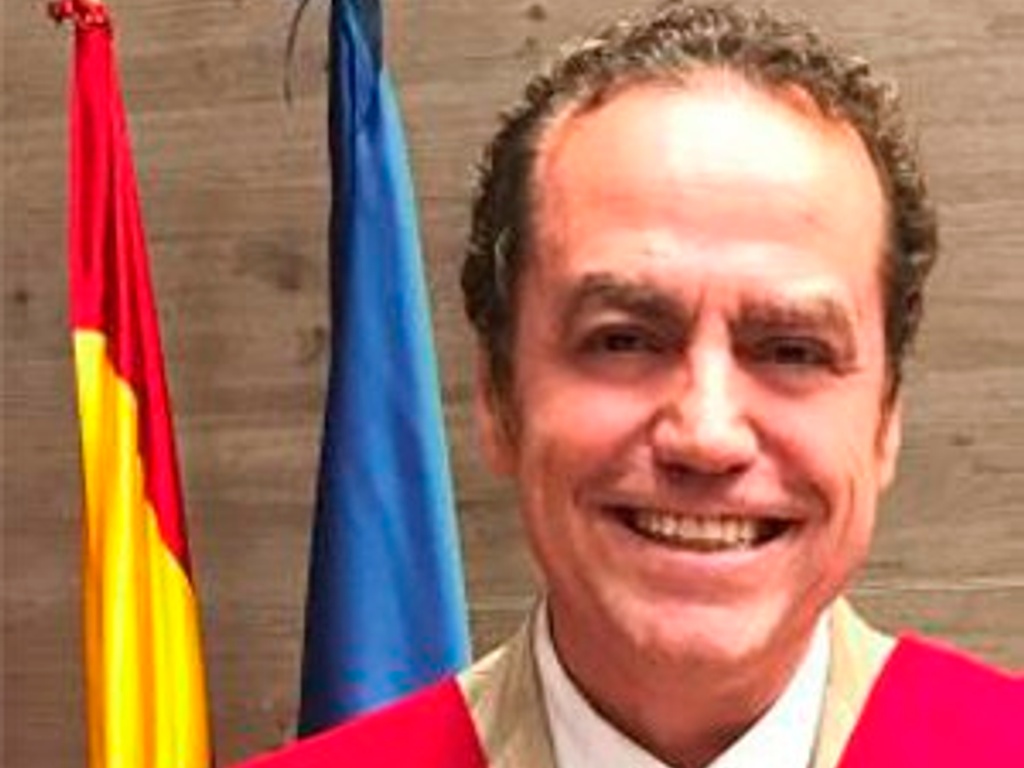 A man in a red robe stands smiling in front of national flags.