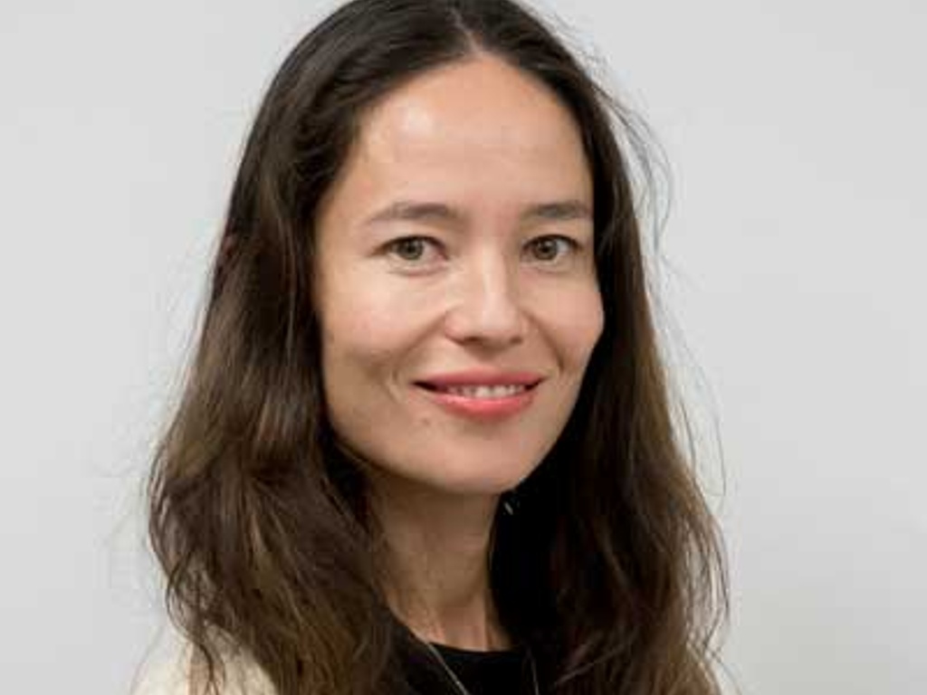 Portrait of a woman with long hair smiling at the camera on a plain background.