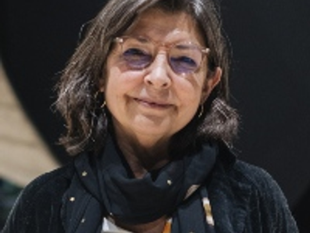 A portrait of a middle-aged woman with glasses, wearing a black scarf and a dark jacket.