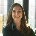 A smiling woman with crossed arms standing in a brightly lit office environment.