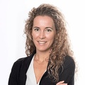 A professional portrait of a smiling woman with curly hair and a black blazer over a white top.