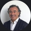 A smiling man with curly hair is wearing a dark suit and white shirt.