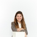A smiling young woman in a plaid blazer stands next to a white pedestal.