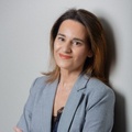 A professional woman in a gray blazer and black top, smiling confidently.