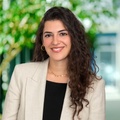 A professional woman with curly hair smiling confidently at the camera in an office environment.