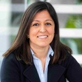 A professional portrait of a smiling woman with long dark hair, wearing a navy blazer and a striped shirt.
