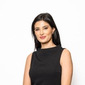 A young woman with long dark hair is smiling while wearing a black sleeveless top.