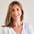 Portrait of a smiling woman with long brown hair wearing a white top.