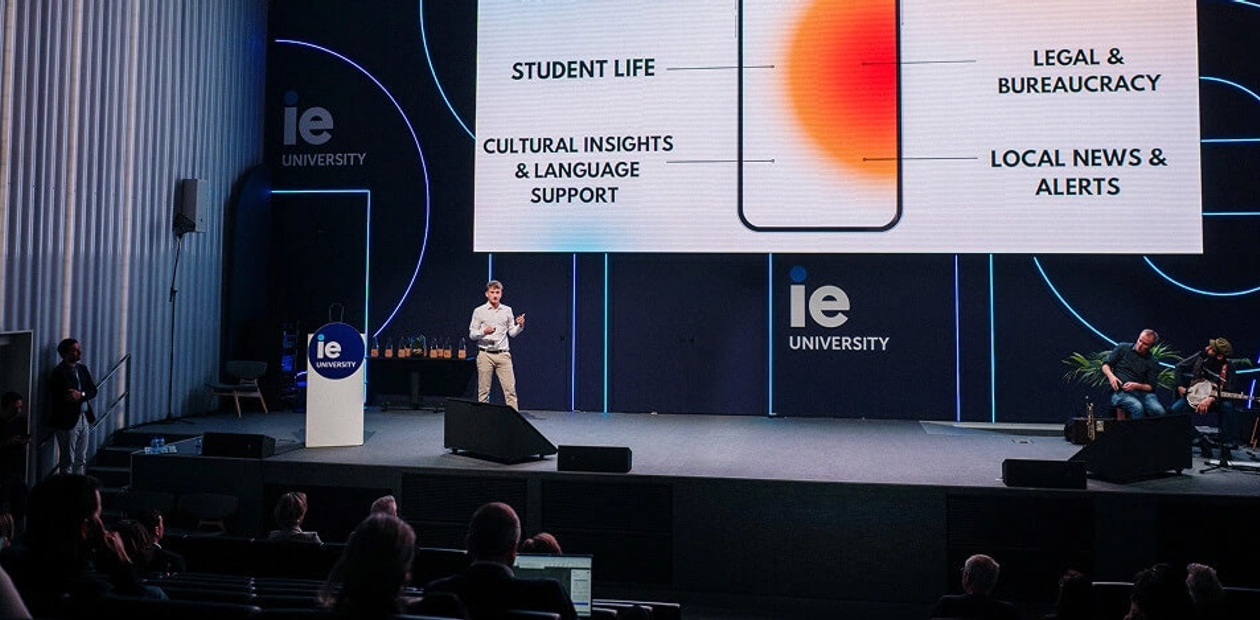 A speaker presents information related to student life and local news at IE University.