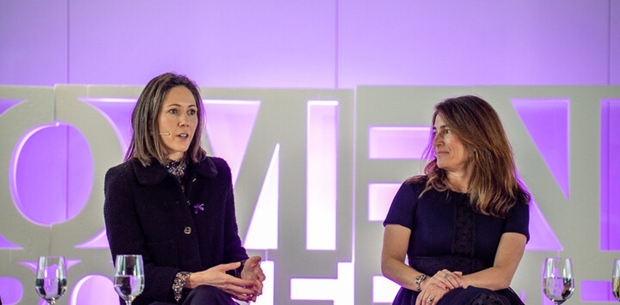 Two women are engaged in a discussion during a panel event with a backdrop that emphasizes women's empowerment.