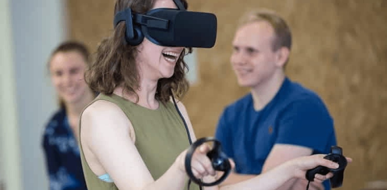 A woman is having fun using a virtual reality headset while two people stand smiling in the background.