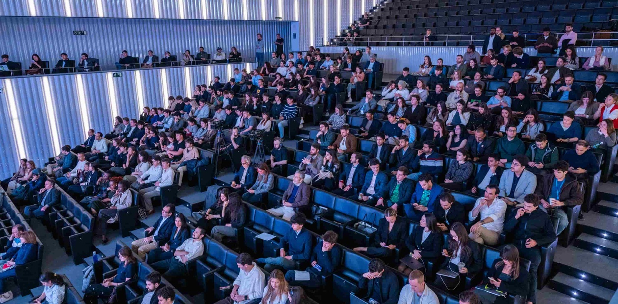 A large audience seated in a modern auditorium with blue lighting.