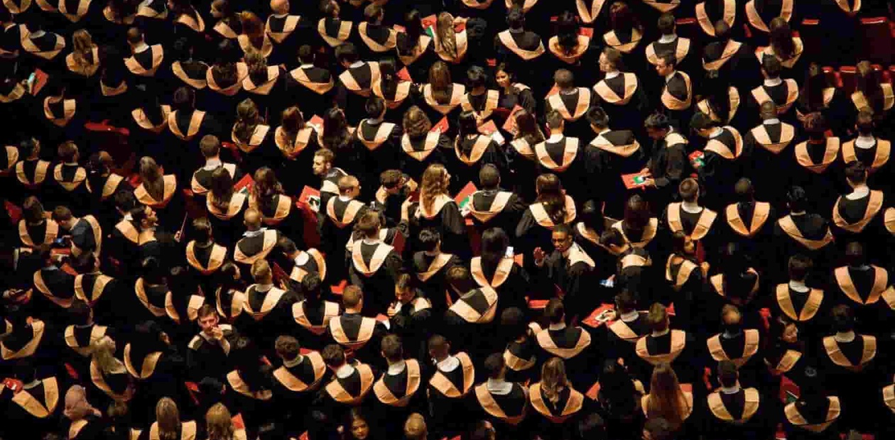 A large group of people in graduation attire holding their hats aloft in celebration.