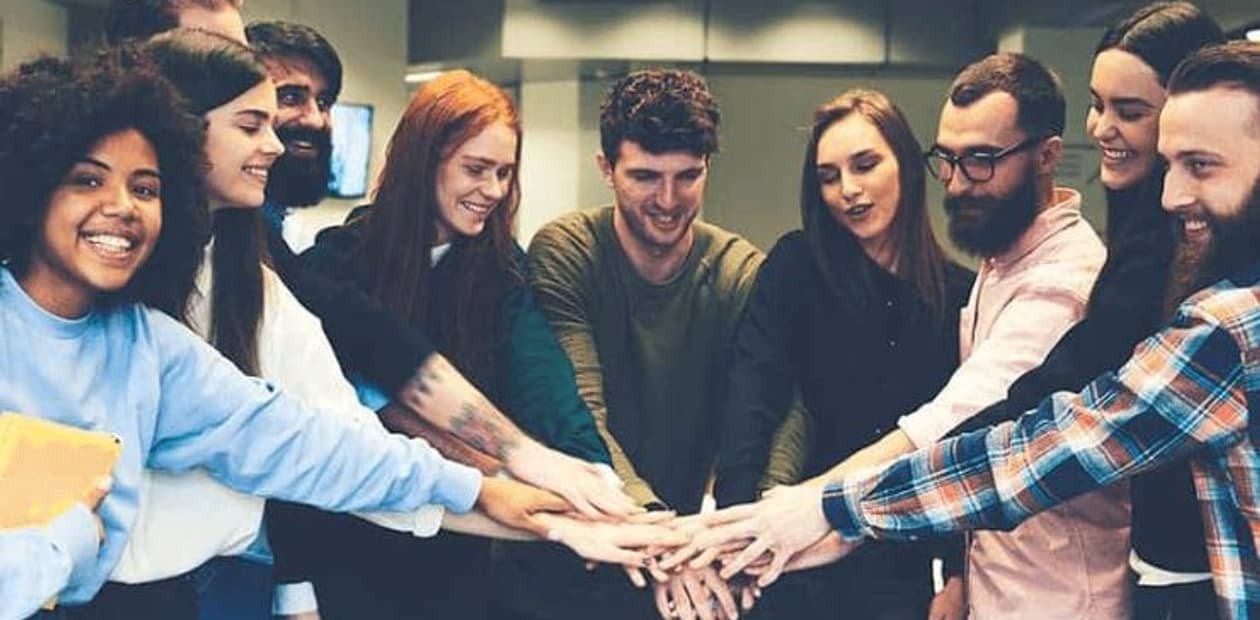 A diverse group of people are smiling and joining hands together in a show of teamwork and unity.