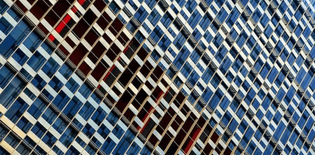 A close-up view of a high-rise building's facade featuring a pattern of blue and red window shades.