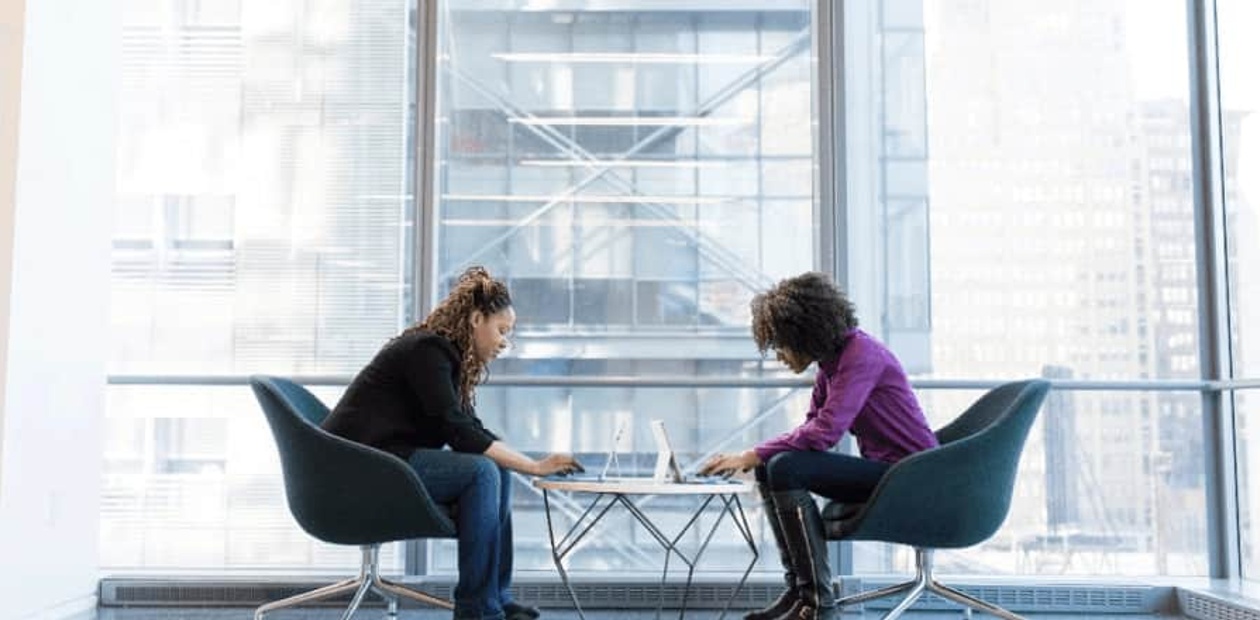 Two women collaborating over a document in a modern office setting with a cityscape background.