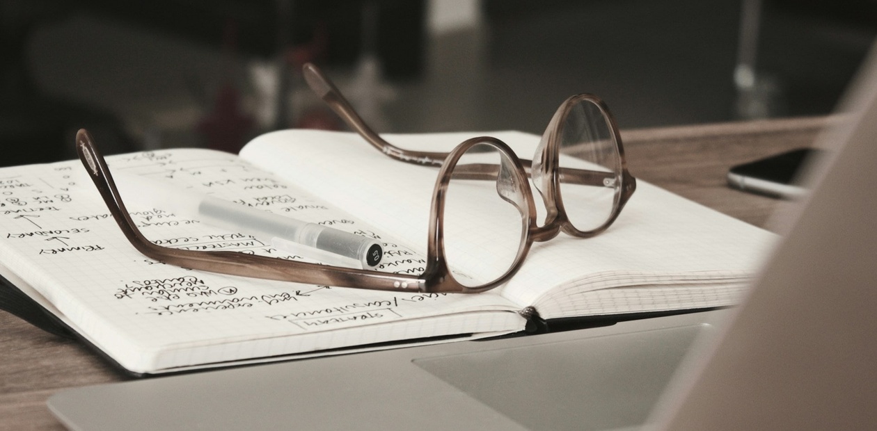A pair of glasses resting on an open notebook with notes and a pen.