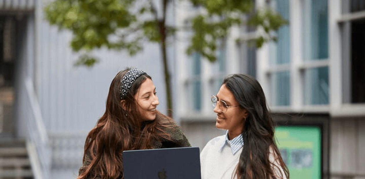 Two women happily discussing over a laptop outdoors in an urban setting.