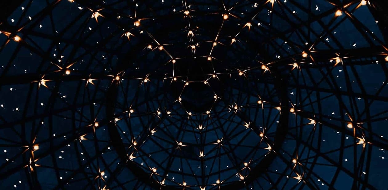 A geometric dome structure illuminated by numerous small lights against a dark sky.