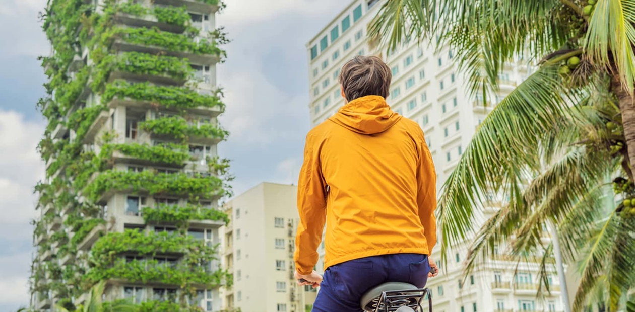 IE student on a bike with a yellow jacket looks at a nature fully covered building