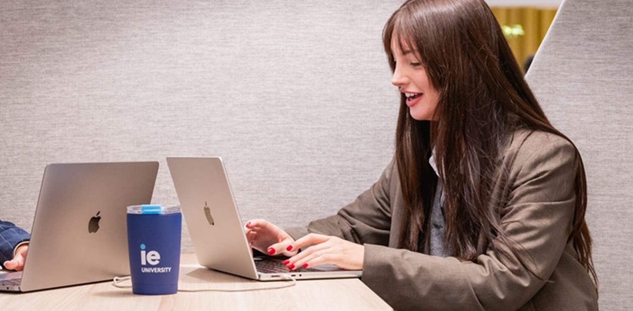 Two students are working on laptops at a table in a modern study space.